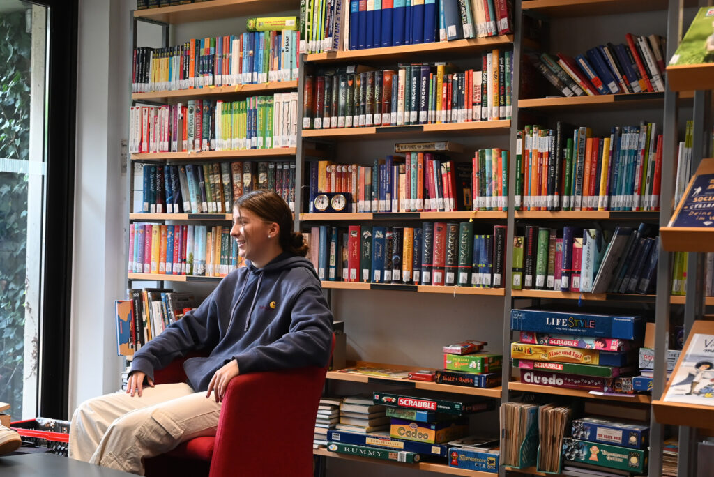 Schülerin sitzt inmitten viele Bücher in der Bibliothek